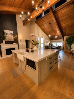 A spacious kitchen with a large island, wooden ceiling beams, and a dining area in the background. - Ultimate Family Retreat | Kids Loft + Firepit (Tulsa)