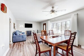 A dining area with a wooden table and chairs, a ceiling fan, and a large window with curtains. - Lakefront four season home w/private beach, boat slip, dock, & fishing kayaks (Ossipee)