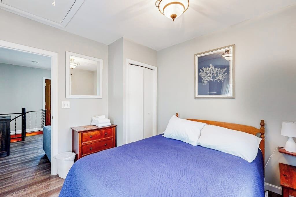 Een slaapkamer met een groot bed, een houten dressoir, een spiegel en een kunstwerk in een lijst aan de muur.