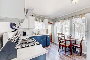 A kitchen with white cabinets, a blue countertop, and a dining area with wooden chairs. - Lakefront four season home w/private beach, boat slip, dock, & fishing kayaks (Ossipee)
