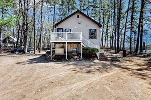 A two-story cabin with a balcony, surrounded by tall trees. - Lakefront four season home w/private beach, boat slip, dock, & fishing kayaks (Ossipee)