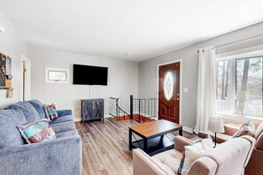 A living room with a sofa, a coffee table, a TV, and a staircase. - Lakefront four season home w/private beach, boat slip, dock, & fishing kayaks (Ossipee)