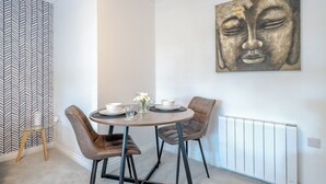Un comedor con una mesa redonda, dos sillas, un jarrón con flores y una obra de arte en la pared.