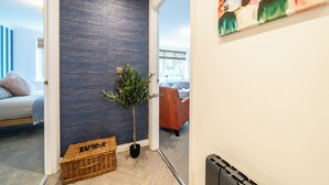 Un pasillo con una pared azul texturizada, una planta en maceta, una cesta de mimbre y un cuadro en la pared.