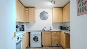 Una cocina compacta con armarios de madera, lavadora, microondas y un reloj en la pared.