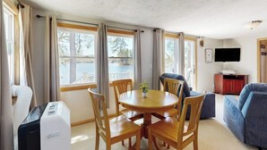 A room with a round wooden table, four chairs, a sofa, a TV, and a heater. - Tranquil lakefront cottage with private beach, boat slip & fishing kayak access (Ossipee)
