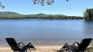 A lake with chairs facing the water, surrounded by trees and hills. - Tranquil lakefront cottage with private beach, boat slip & fishing kayak access (Ossipee)
