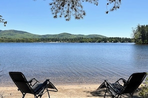 A lake with chairs facing the water, surrounded by trees and hills. - Tranquil lakefront cottage with private beach, boat slip & fishing kayak access (Ossipee)