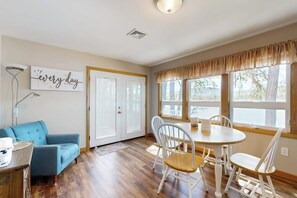 A room with a dining table, chairs, a blue sofa, a white cabinet, and a window with curtains. - Lakefront home with private beach, access to dock/fishing/kayaks/boat slip (Ossipee)