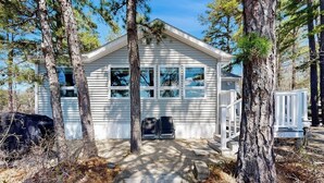 A small, single-story cabin with a porch, surrounded by trees. - Lakefront home with private beach, access to dock/fishing/kayaks/boat slip (Ossipee)