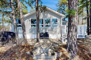 A small, single-story cabin with a porch, surrounded by trees. - Lakefront home with private beach, access to dock/fishing/kayaks/boat slip (Ossipee)