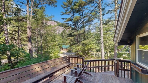 Eine Holzterrasse mit Bänken und einem Schaukelstuhl, mit Blick auf eine bewaldete Gegend und einen Berg im Hintergrund.