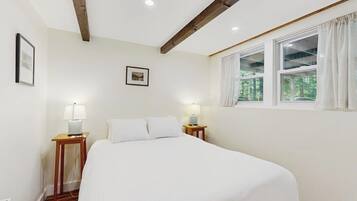 Une chambre à coucher avec un lit, deux tables de chevet avec des lampes, une fenêtre avec des rideaux et un tableau encadré au mur.