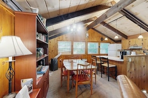 A cozy cabin interior with a dining area, kitchen, and a bookshelf.