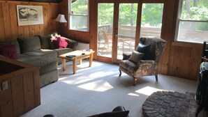 Ein gemütliches Blockhaus-Interieur mit Holzboden, einer Couch, einem Sessel, einem Couchtisch und einem Kamin.