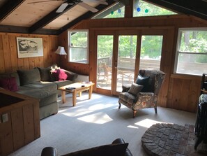 A cozy cabin interior with a wooden floor, a sofa, a chair, a coffee table, and a fireplace.