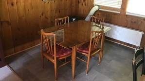 Ein Zimmer mit Holzwänden, einem Esstisch, vier Stühlen, einer Heizung und einem Fenster mit Jalousien.