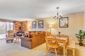 Ein Wohnzimmer mit Backsteinwand, einer Couch, einem Esstisch mit Stühlen, einer Pendelleuchte und einem großen Fenster.