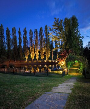 Un espace extérieur aménagé pour la nuit, avec un chemin en pierre, des arbres et une clôture.