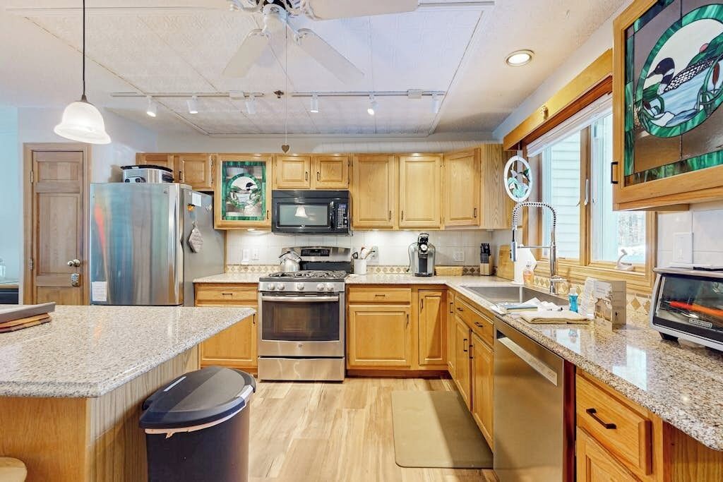 Cocina con armarios de madera, electrodomésticos de acero inoxidable y encimeras de granito, además de un ventanal con vistas decorativas.