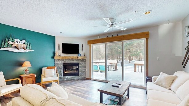 A living room with a fireplace, a ceiling fan, and a large sliding glass door leading to an outdoor area. - Mountain condo: centrally located to shopping, restaurants, skiing, hike & more (North Conway)