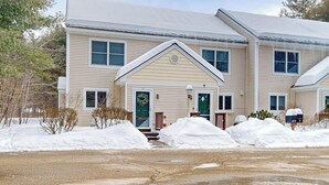 A two-story building with a symmetrical facade, a central entrance with steps, and a snow-covered ground. - Mountain condo: centrally located to shopping, restaurants, skiing, hike & more (North Conway)