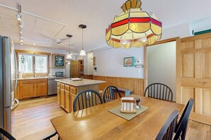 Eine Küche mit Holzausstattung, einem Esstisch mit Stühlen, einer Pendelleuchte und einem Kühlschrank.