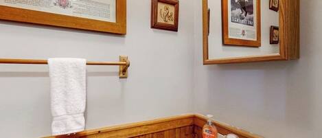 Une salle de bain avec un meuble-lavabo en bois, un lavabo blanc, un porte-serviettes et des affiches encadrées au mur.