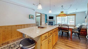 A kitchen with wooden cabinets, a granite countertop, a dining area with chairs, and pendant lighting. - Mountain condo: centrally located to shopping, restaurants, skiing, hike & more (North Conway)