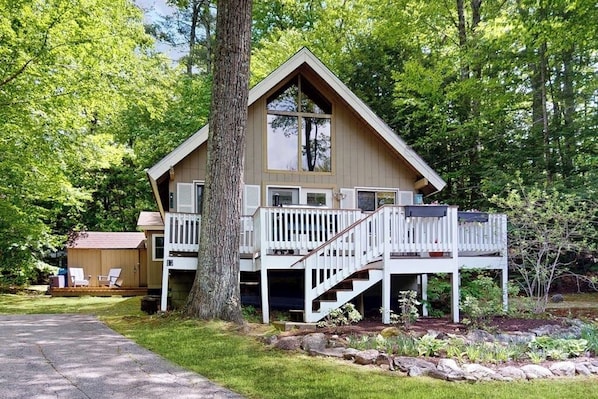 A two-story cabin with a balcony, surrounded by trees. - Country dog friendly lake house w/ access to beaches, tennis & pickleball (Tuftonboro)