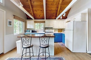 A kitchen with wooden beams, white cabinets, a blue island, and two bar stools. - Country dog friendly lake house w/ access to beaches, tennis & pickleball (Tuftonboro)
