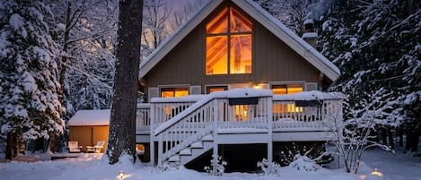 Een chalet met een groot raam, een terras en een besneeuwde omgeving.