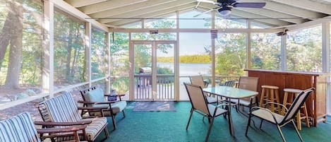 A covered patio with seating, a table, and a bar area, overlooking a body of water.
