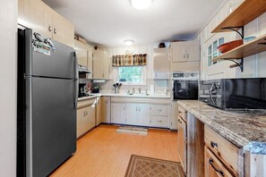 A kitchen with light wood cabinets, a black refrigerator, a microwave, and a window with curtains. - Lakefront cottage on Big Pea Porridge Pond w/ private dock, beach, kayaks, canoe (Madison)