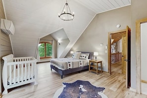 A bedroom with a sloped ceiling, a bed, a white crib, a nightstand, and a view of greenery outside. - Spectacularly updated family mountain lodge w/deck & amazing views (Madison)