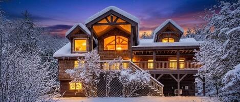 A log cabin with a warm interior light, surrounded by snow-covered trees.
