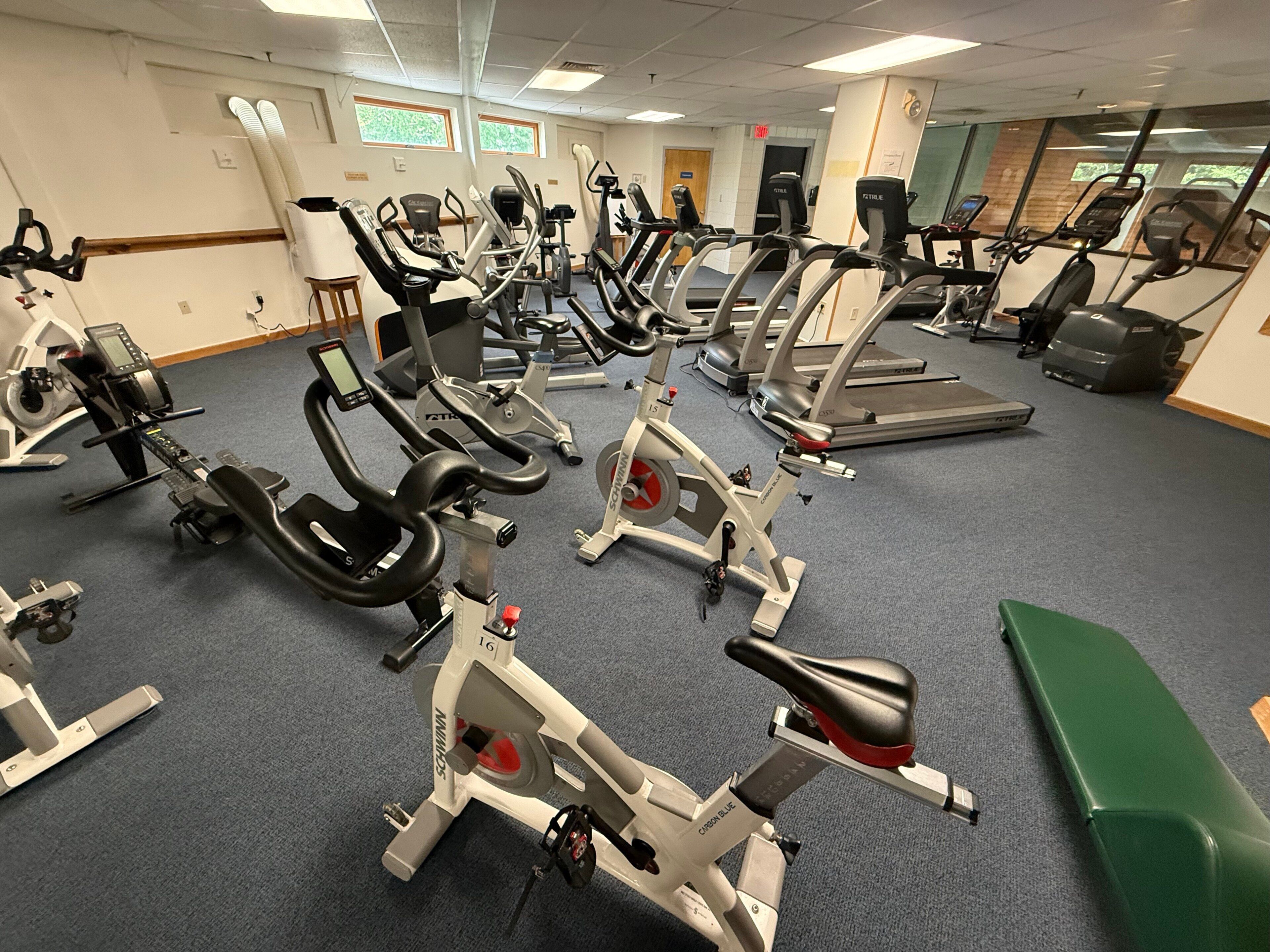 Une salle de sport équipée de divers appareils d’exercice, notamment des tapis de course et des vélos d’appartement, disposés en rangées.
