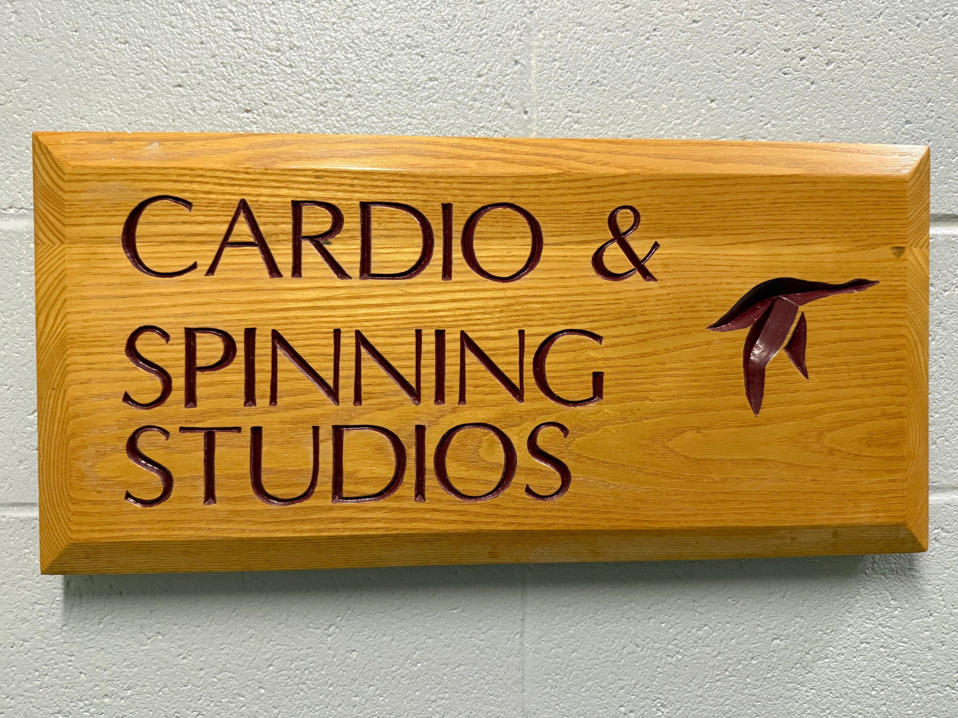 A wooden sign with the text 'CARDIO & SPINNING STUDIOS' and a silhouette of a spinning figure.