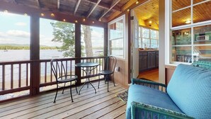 A wooden deck with a table and chairs, a sofa, and a view of a body of water.