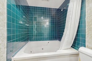 Ein Badezimmer mit einer Badewanne, einer weißen Toilette und wandhoch gefliesten tealfarbenen Fliesen.