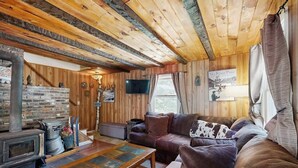 Interior acogedor de una cabaña con chimenea, paredes de madera, un sofá y un televisor.
