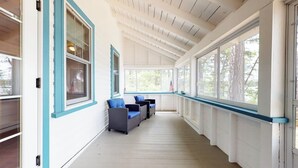 Une véranda couverte aux murs blancs et aux bordures bleues, agrémentée d’une rangée de fenêtres et d’un espace salon avec deux chaises et une table.