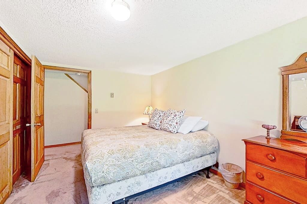 Ein Schlafzimmer mit Bett, Kommode, Spiegel und einer Tür zu einem anderen Raum.