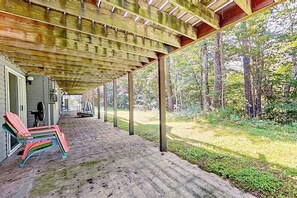Un espacio al aire libre techado, con suelo de concreto, vigas de madera y vistas a un bosque.