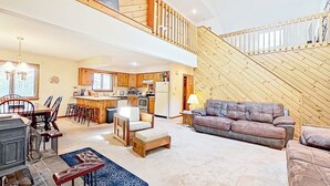 A spacious living area with a high ceiling, a dining table, a sofa, and a kitchen in the background.
