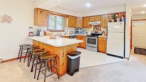 A kitchen with wooden cabinets, a central island with stools, a stove, microwave, and refrigerator.