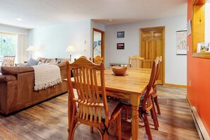 Ein Essbereich mit Holztisch und Stühlen, einer Couch mit Decke und einer Tür mit Spiegel.