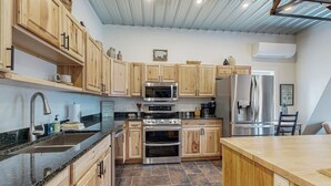 A modern kitchen with wooden cabinets, a granite countertop, stainless steel appliances, and a tiled floor.