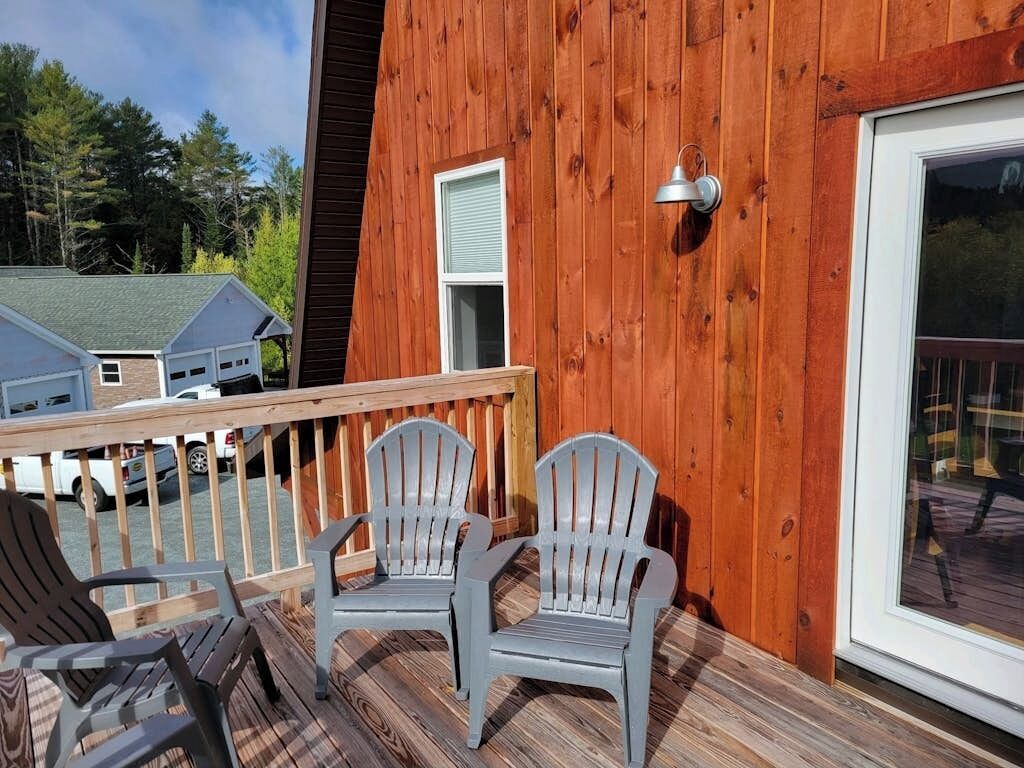 Puinen terassi, jossa on Adirondack-tyyliset tuolit, kaide ja ikkuna, jonka yläpuolella on metallinen valaisin.