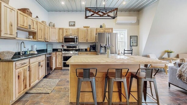 A kitchen with wooden cabinets, a central island with stools, a hanging light fixture, and a microwave.